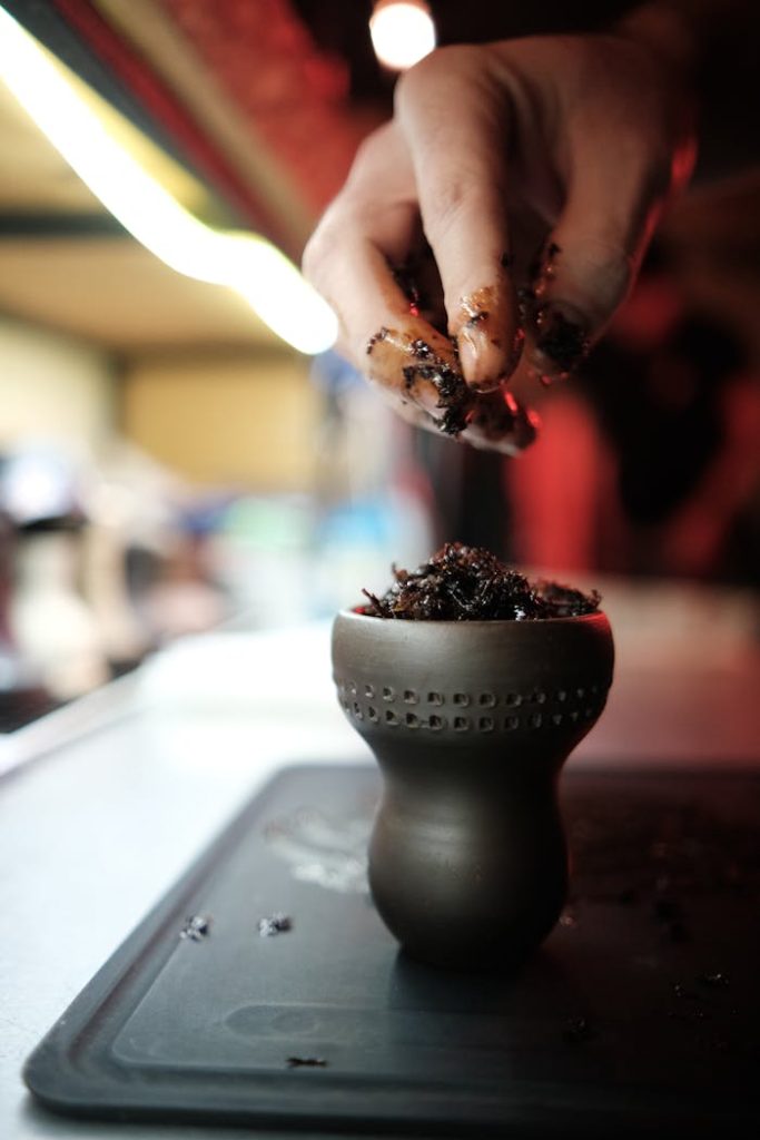 Close-up of a hand preparing hookah tobacco in a clay bowl, emphasizing texture and technique.