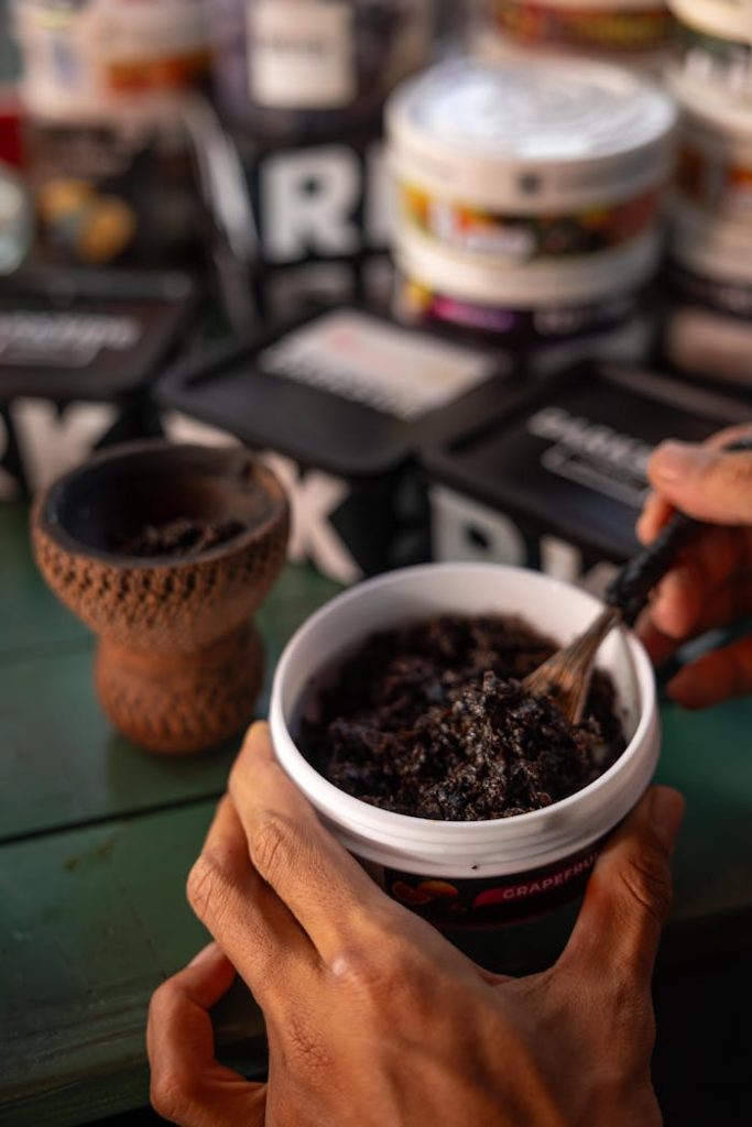 Hands preparing hookah tobacco with a clay bowl on a green table.